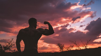 Wall Mural - a silhouetted muscular man flexes his bicep against a vibrant and dramatic sunset sky with sparse vegetation in the foreground.
