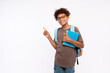 © InsideCreativeHouse - Smiling African-American preteen boy male elementary primary school pupil holding copybooks with backpack showing pointing index finger at copy space for promotional ad on white background.
