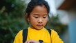 © Z A C - A young girl looking at a device while standing outside.