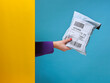 © French Anderson Ltd/Stocksy - Woman’s hand holding parcel from behind yellow wall.