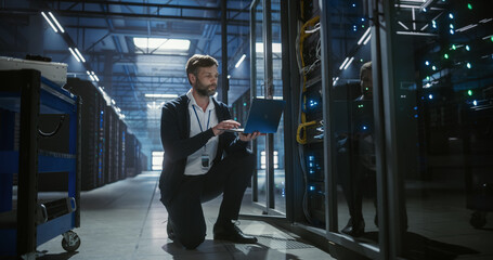 IT specialist working on laptop in data center.