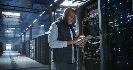 Data center technician inspects server racks, checks network cables.