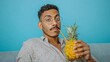 © Nataliia_Trushchenko - Man with glasses is holding a pineapple and straw. He is sitting on a couch. The image conveys a relaxed and casual atmosphere