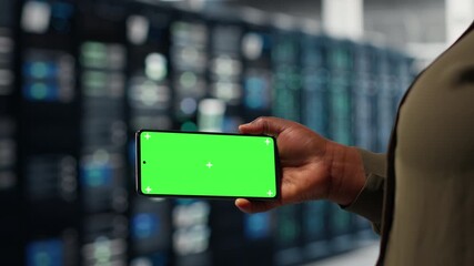 Software developer using app on mockup phone to check server hub energy consumption. African american woman using green screen smartphone in data center to do gear checkup, camera B
