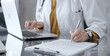 © volha_r - Doctor woman is writing on a document on a glass desk, with a laptop and tablet visible. Work space concept in Medicine