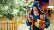 © Home-stock - Modern holiday shopping. Happy lady holding gift boxes and using smartphone while standing outdoors near Xmas tree and festive decorations