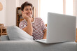 © Pixel-Shot - Young man video chatting with laptop on sofa at home