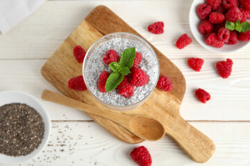 Wall Mural - glass of tasty chia seed pudding with fresh raspberries and mint on white wooden background