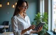 © Susan - European businesswoman CEO using fintech tab application standing at workplace in office. Latin Hispanic mature professional business woman holding digital tablet for trading, looking at copy space