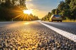© Ninth - Asphalt highway at sunset. Sunlight beams down on a road with a car driving away