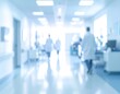 © belva - Blurred long hospital corridor with white walls, bright lighting, and figures in white coats walking away in the distance