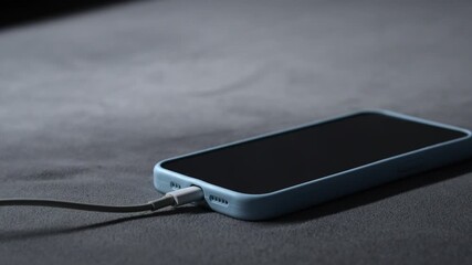 A mobile phone in a blue case is charging.
The smartphone is charging from a wall outlet using a power cord.
A power cord connected to the smartphone provides fast charging.
