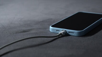 A mobile phone in a blue case is charging.
The smartphone is charging from a wall outlet using a power cord.
A power cord connected to the smartphone provides fast charging.