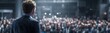 © gina - Speaker addresses a large, blurry crowd from a stage; back view of the presenter. Audience is dark and indistinct