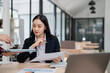 © MINAE - Two asian businesswomen are having a meeting in a modern office, analyzing financial charts and company's marketing strategy, working together using laptop and documents