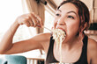 © EdNurg - Young woman is very hungry and greedily eating spaghetti with a fork from plate in a restaurant