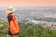© EdNurg - Female hiker shielding her eyes from the sun while admiring a cityscape from a mountain viewpoint