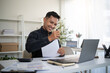 © matinee - Happy businessman smiling while stamping documents at modern office desk with laptop.