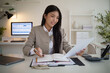 © matinee - Confident businesswoman working on financial or business documents at modern office.