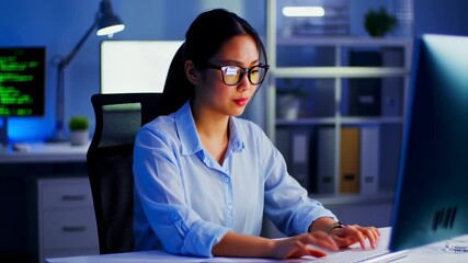 Focused Asian programmer working late night coding and analyzing data on computer screen