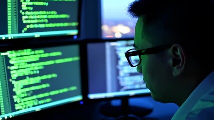 Dedicated programmer intensely working on multiple monitors full of green lines code