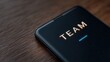 © FocusFusion - Mobile Device With Team Message on Wooden Table