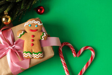 Wall Mural - Saint Nicholas day. Gingerbread man, candy canes, fir tree, ornaments and gift box on green background, flat lay