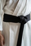 A white judo gi worn by a practitioner of martial arts, featuring a black obi belt tied in a knot on the waist.