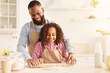 © Prostock-studio - Home Bakery Concept. Happy african american man and his child daughter rolling up dough with pin together, having fun, daddy and daughter making cookies, cake, bread or preparing pizza, copy space