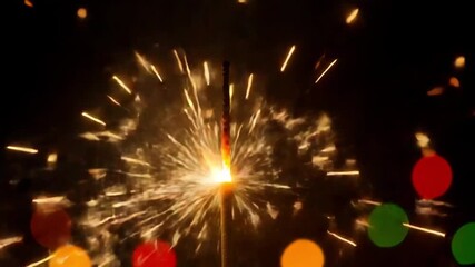 A single sparkler bursts with golden light, illuminating the darkness with a shower of shimmering sparks and bokeh lights in the foreground