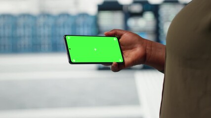 Close up of engineer using app on mockup phone to check server farm energy consumption. System administrator using green screen smartphone in data center to do infrastructure checkup