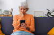 © Xavier Lorenzo - Worried senior woman reading bad news on smart phone message sitting on sofa at home.