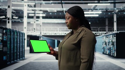 IT professional in data center using green screen tablet to ensure error free supercomputers networks. African american woman uses mockup device to monitor server hub gear parts for failures, camera A