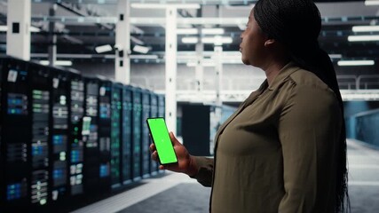 Software developer using app on mockup phone to check server hub energy consumption. African american woman using green screen smartphone in data center to do gear checkup, camera A