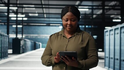 Data center software developer monitors data center metrics on tablet to enhance operational effectiveness. Woman in server room using app device analytics to predict performance, camera B