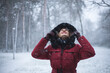 © K&M FEHR - Portrait of beautiful young woman in red winter hooded jacket, while looking and and cheerful watching snowflakes falling all around. Fashion model in winter scene forest, snowing, Christmas, season.