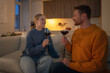 © DimaBerlin - Laughing couple drinking wine on sofa looking at each other lovingly in intimate light. Romantic evening, emotional connection, love relationship, man and woman bonding at home, date on weekends