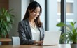 © li - Smiling mature Asian professional it specialist businesswoman working on laptop pc standing in office workplace. 30s middle-aged woman using computer technology app for banker financial work online.