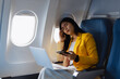© NanSan - A young Asian businesswoman sits inside an airplane, suffering from nausea, headache,stomach discomfort during a long flight, appearing exhausted and stressed, illustrating the physical challenges