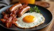 © Pete - Crispy bacon, juicy sausages, and sunny-side-up egg on black plate. Inviting breakfast setup. Homestyle meal, perfect for morning brunch, offering comfort and warmth with every savory bite.