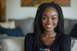 © Kru Kapur - Portrait of a young successful African American woman at home, smiling and looking at the camera, holding a phone while sitting on the couch in the living room, Generative AI