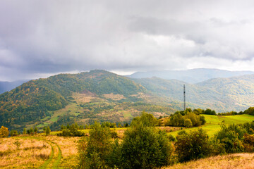 Wall Mural - autumn landscape in mountains. beautiful view of countryside in europe. colorful carpathian alps of ukraine in the background. cloudy sky. picturesque rural scenery with village in the valley