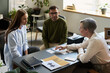 © Mediaphotos - Middle aged woman psychologist conducting therapy session with young woman and young man, explaining psychological concepts using paper cards