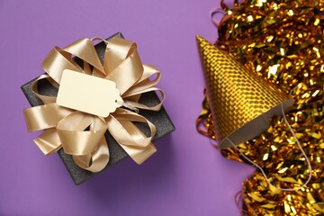 Wall Mural - Gift box with blank tag and festive decor on purple background, flat lay