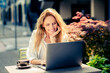 © deagreez - Charming mature woman enjoying relaxation outdoors while working on a laptop in a sunlit urban area during spring