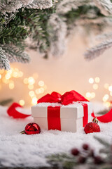 Wall Mural - white gift box with red ribbon and ornaments under snowy branches, set against warm holiday lights. 