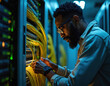 © Vadym - Focused African American man works with server cables in a data center at night. He handles wires, dealing with networking hardware. The scene shows IT work and technology.