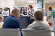© DC Studio - Receptionist at front desk supports patient intake by updating health records and scheduling treatment visits in busy clinic. Hospital staff discussing upcoming medical checkups with asian man.