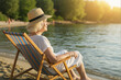 © Milan - Senior woman relaxing in a deck chair on the beach at sunset. Mature person enjoying a summer vacation. Retirement and leisure lifestyle concept.