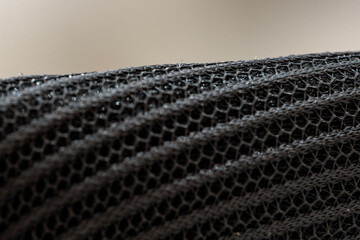 Extreme close-up of a black synthetic mesh fabric with a hexagonal net pattern. Abstract industrial background with selective focus and texture.